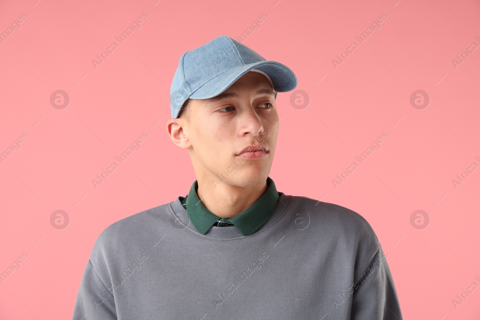 Young man in stylish baseball hat on pink background Photo of Young man in stylish baseball hat on pink background