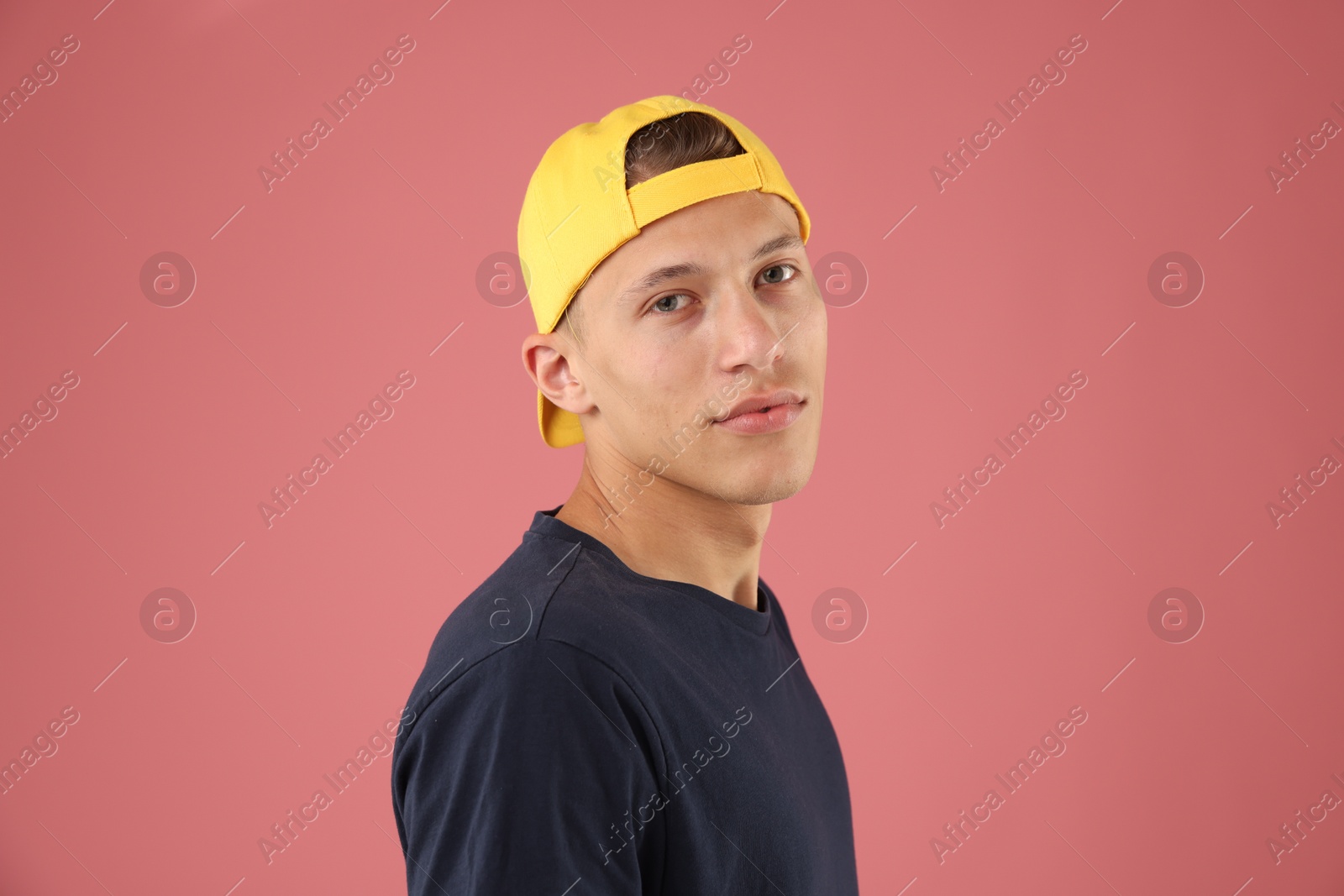 Young man in stylish baseball hat on pink background Photo of Young man in stylish baseball hat on pink background