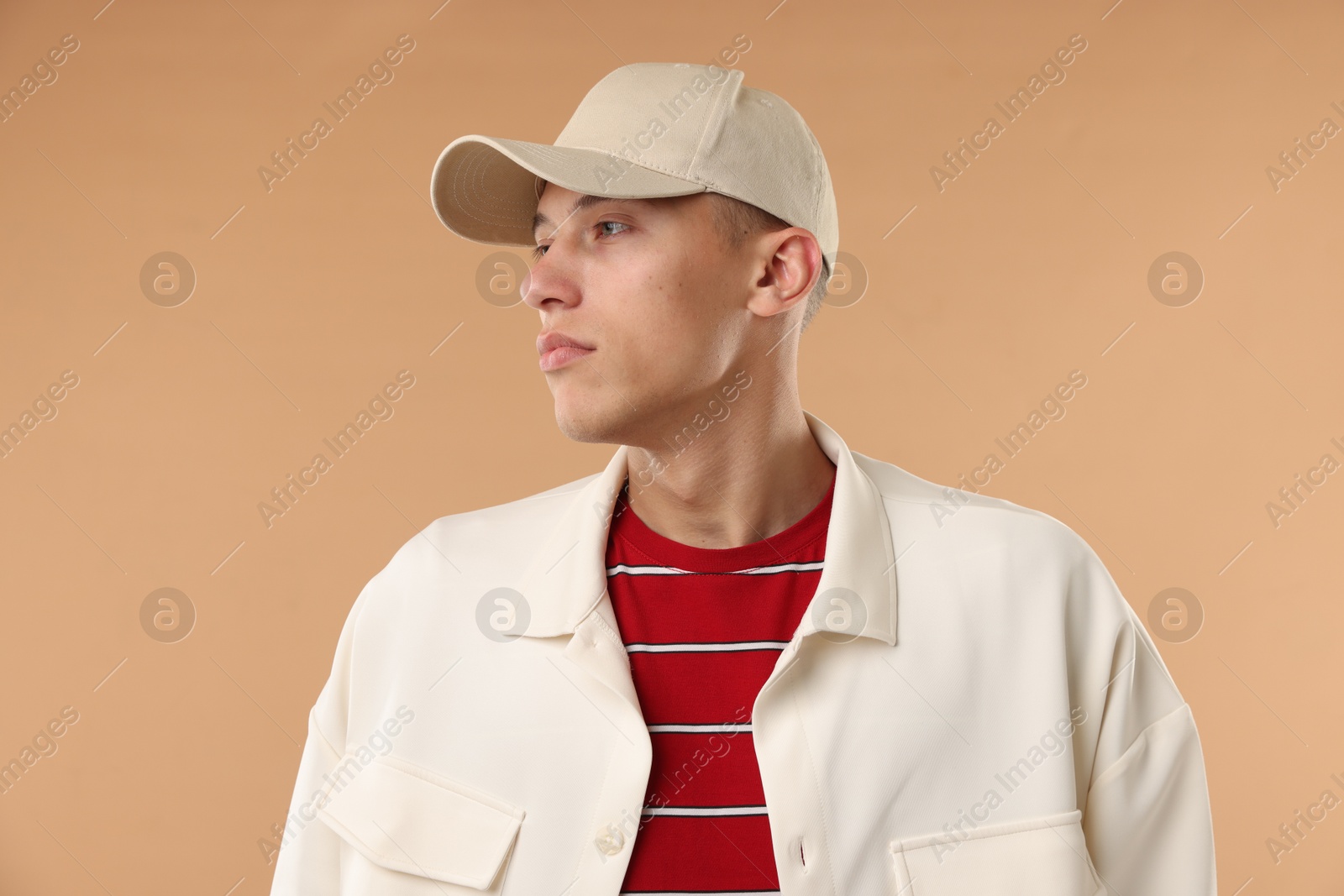 Young man in stylish baseball hat on beige background Photo of Young man in stylish baseball hat on beige background