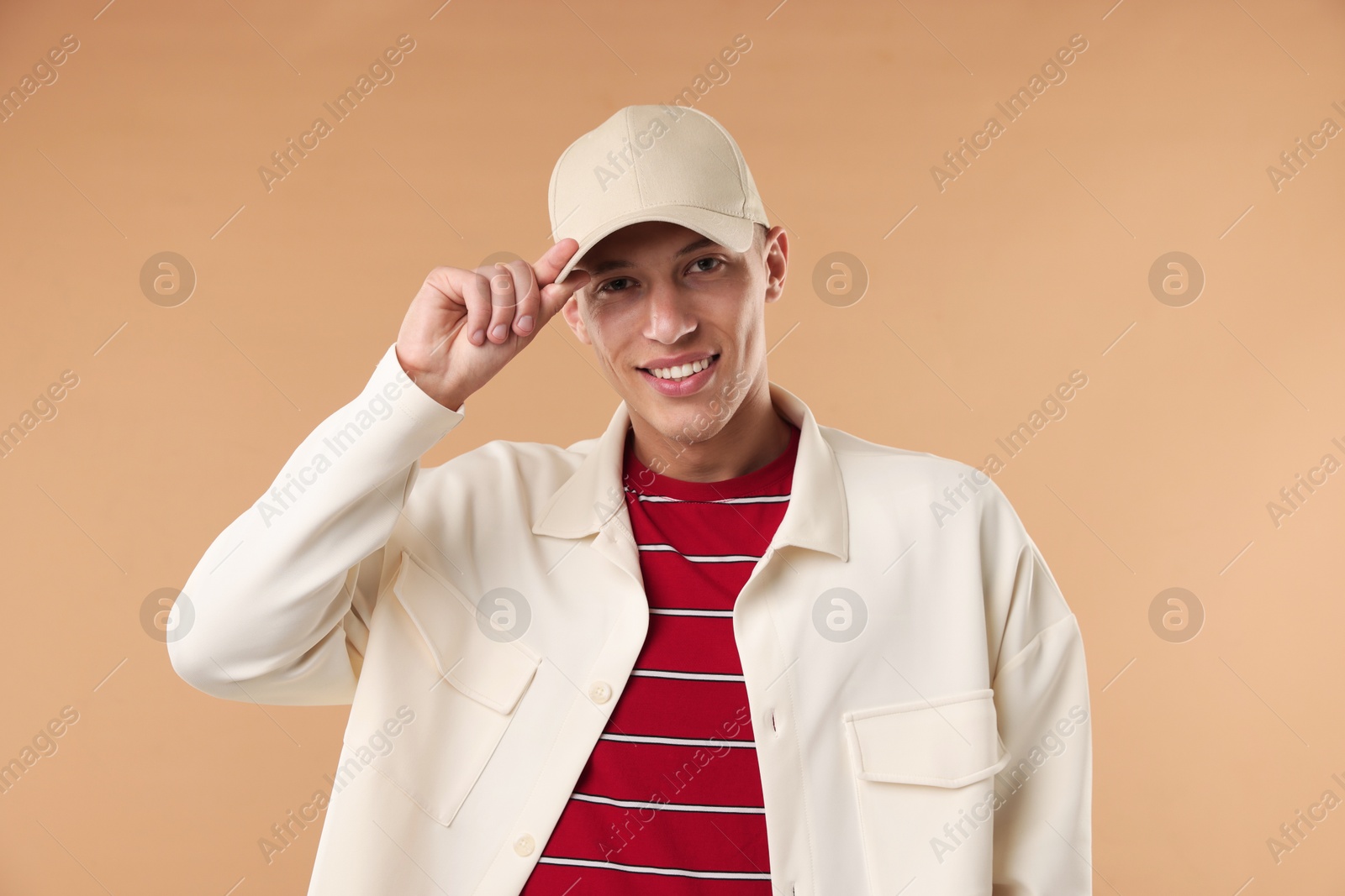 Young man in stylish baseball hat on beige background Photo of Young man in stylish baseball hat on beige background