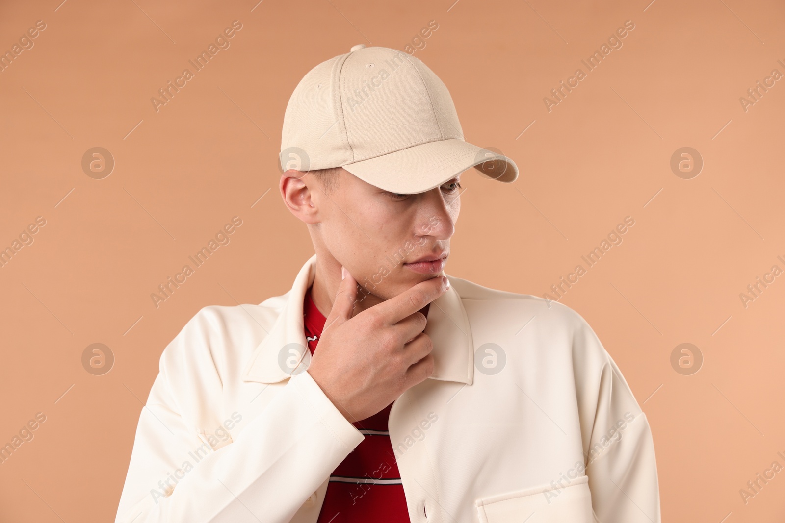 Young man in stylish baseball hat on beige background Photo of Young man in stylish baseball hat on beige background
