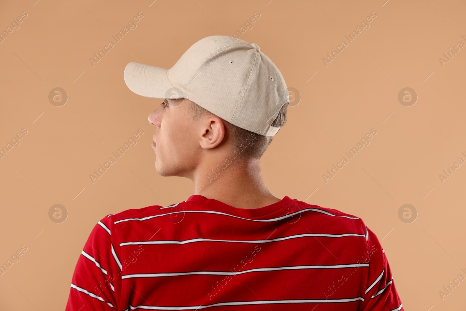 Young man in stylish baseball hat on beige background Photo of Young man in stylish baseball hat on beige background