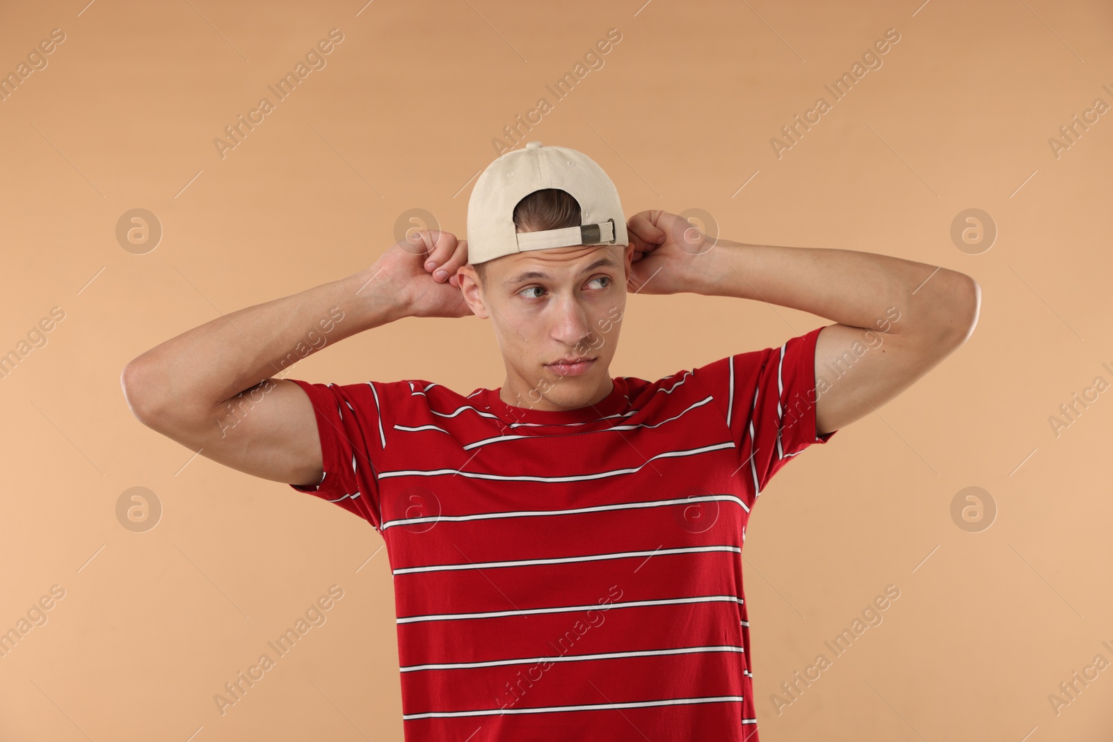 Young man in stylish baseball hat on beige background Photo of Young man in stylish baseball hat on beige background