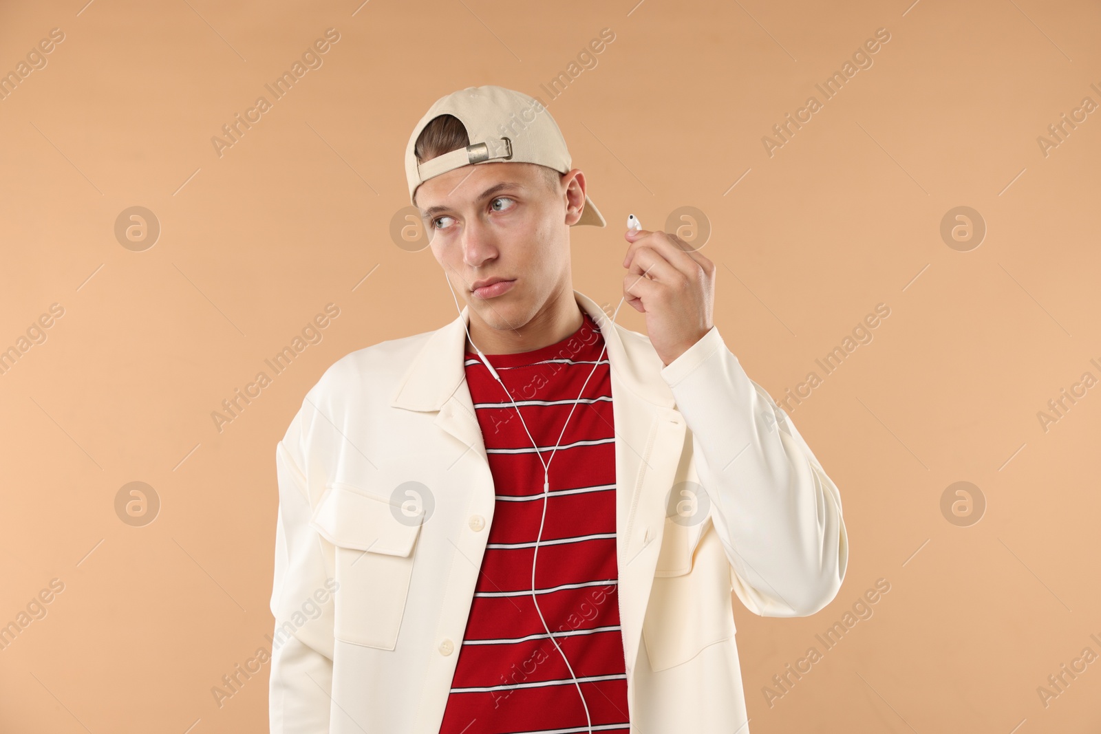 Young man in stylish baseball hat with earphones on beige background Photo of Young man in stylish baseball hat with earphones on beige background