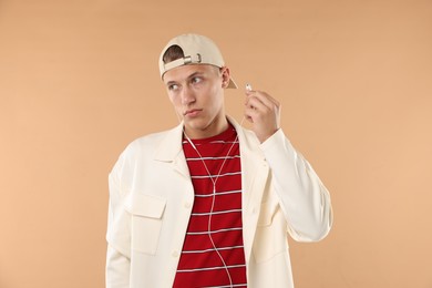 Photo of Young man in stylish baseball hat with earphones on beige background