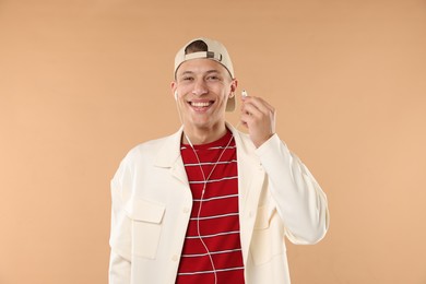 Photo of Young man in stylish baseball hat with earphones on beige background