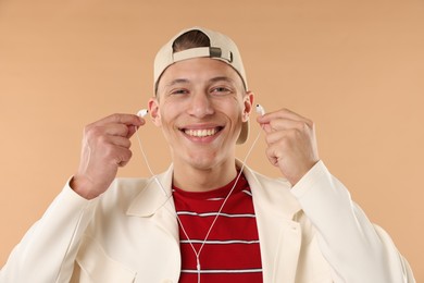 Photo of Young man in stylish baseball hat with earphones on beige background