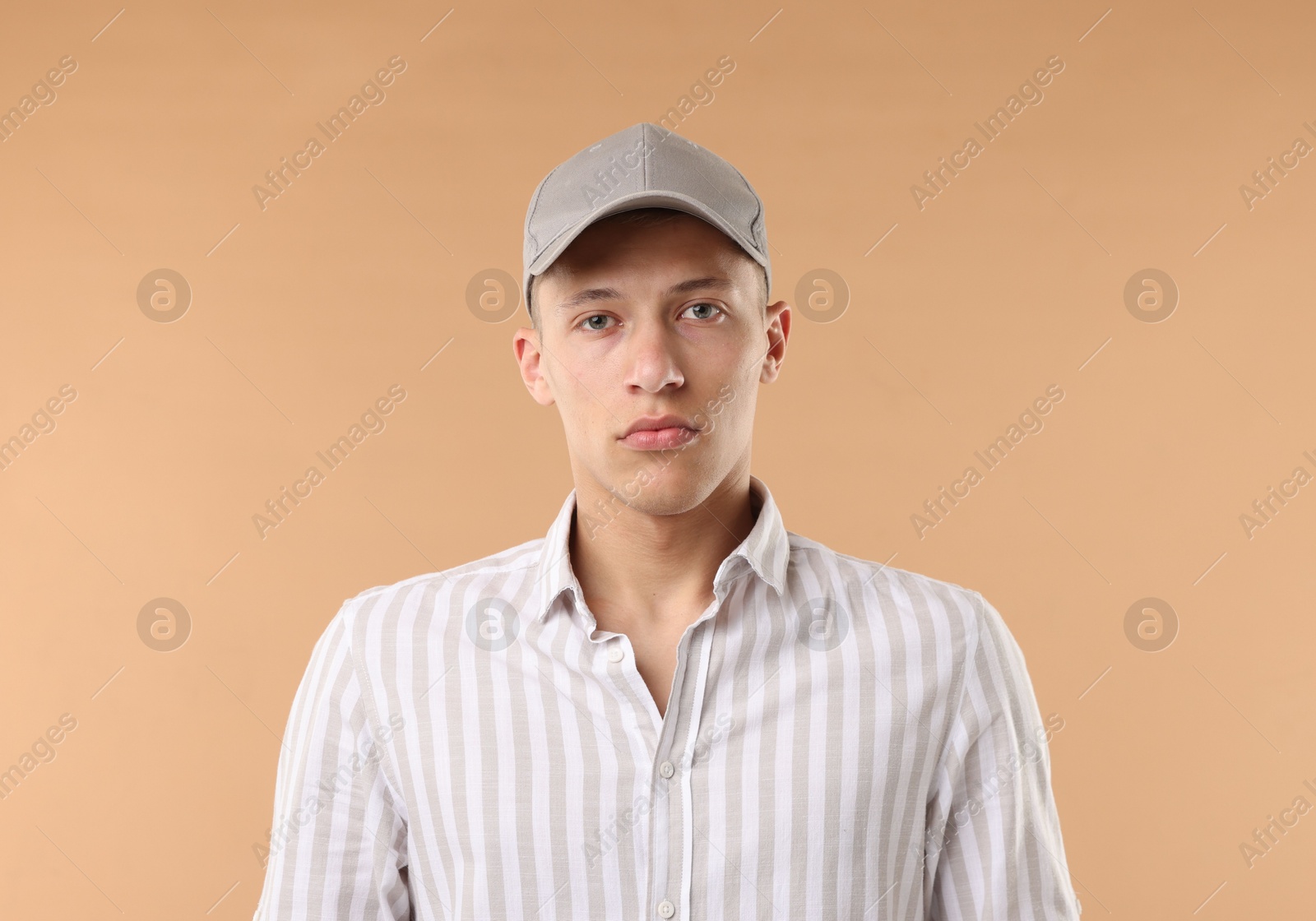 Young man in stylish baseball hat on beige background Photo of Young man in stylish baseball hat on beige background
