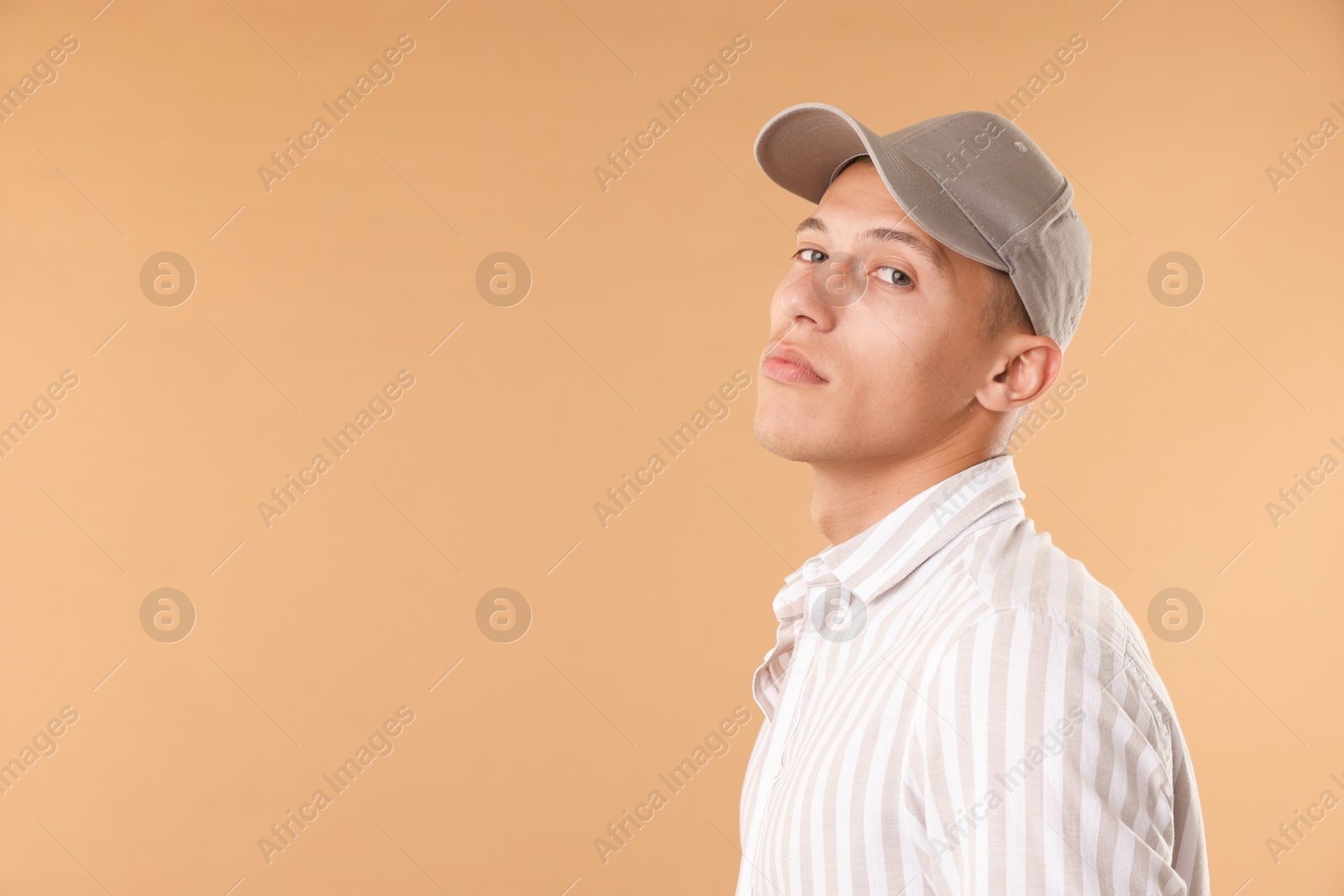 Young man in stylish baseball hat on beige background, space for text Photo of Young man in stylish baseball hat on beige background, space for text