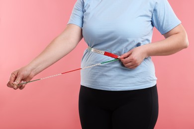 Photo of Weight loss. Plus size woman measuring waist with tape on pink background, closeup