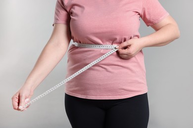 Photo of Weight loss. Plus size woman measuring waist with tape on gray background, closeup