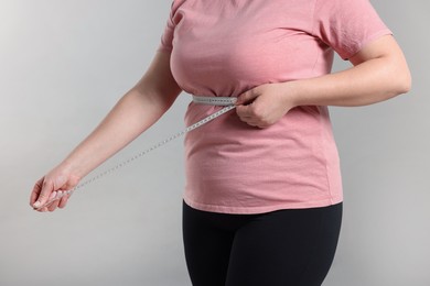 Photo of Weight loss. Plus size woman measuring waist with tape on gray background, closeup