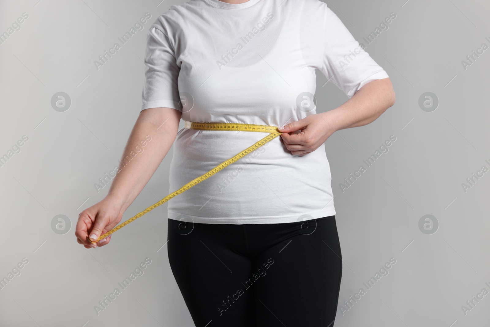 Weight loss. Plus size woman measuring waist with tape on gray background, closeup Photo of Weight loss. Plus size woman measuring waist with tape on gray background, closeup
