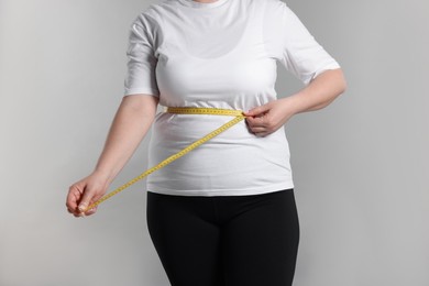Photo of Weight loss. Plus size woman measuring waist with tape on gray background, closeup