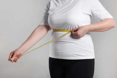 Photo of Weight loss. Plus size woman measuring waist with tape on gray background, closeup