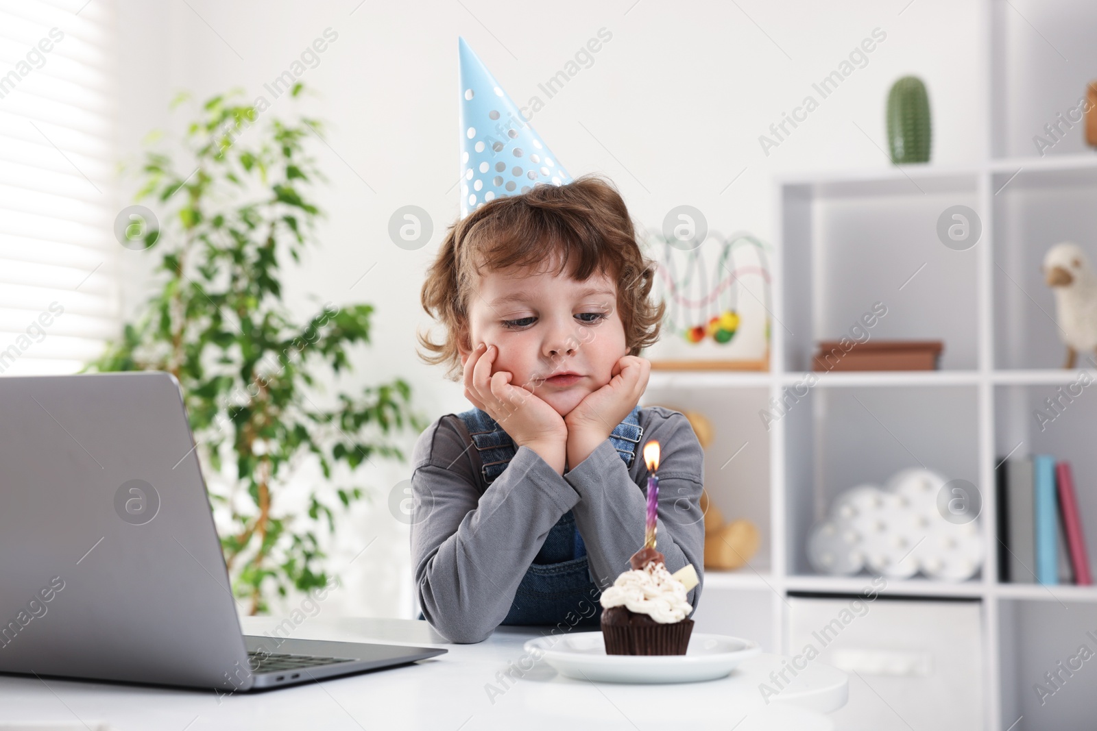 Birthday celebration. Little boy with cupcake having video call via laptop at table indoors Photo of Birthday celebration. Little boy with cupcake having video call via laptop at table indoors