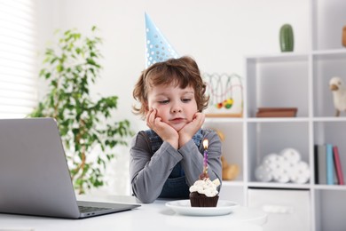 Photo of Birthday celebration. Little boy with cupcake having video call via laptop at table indoors