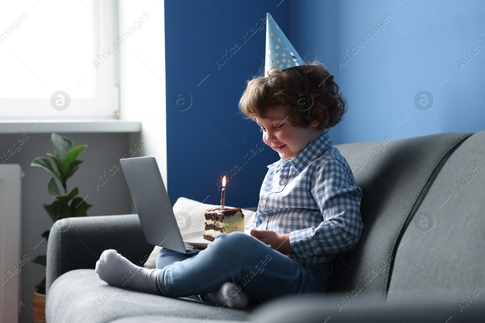 Birthday celebration. Little boy with piece of cake having video call via laptop on sofa at home Photo of Birthday celebration. Little boy with piece of cake having video call via laptop on sofa at home