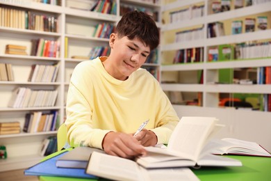 Photo of Student with books studying at table in library