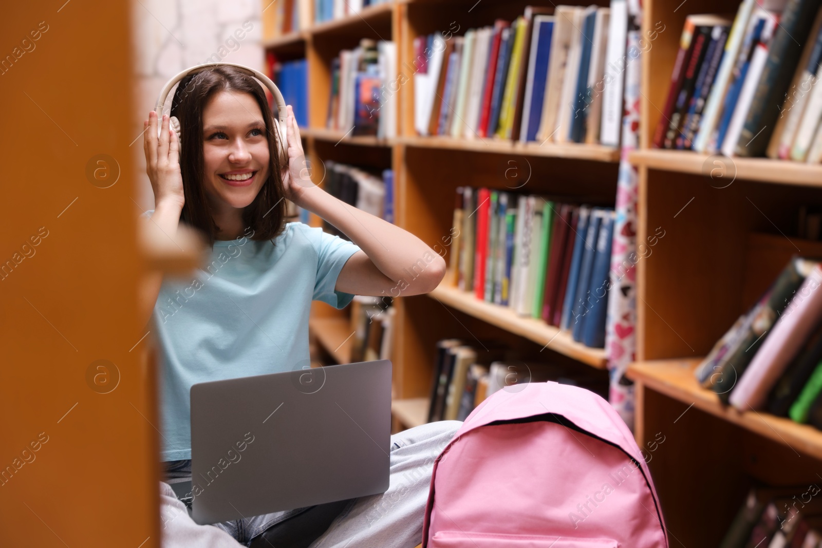 Photo of Student with laptop and backpack between shelves in library