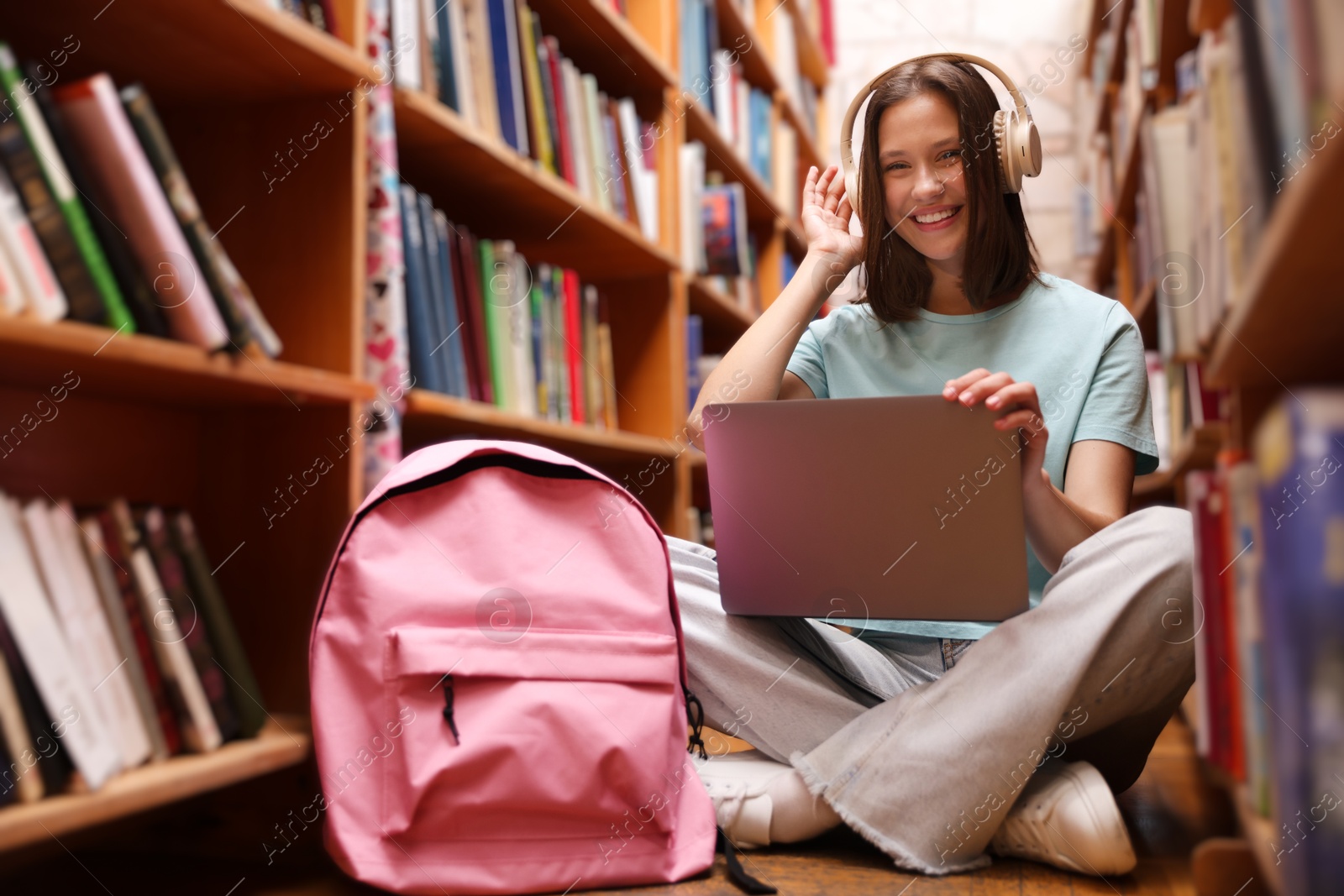 Student with laptop and backpack between shelves in library Photo of Student with laptop and backpack between shelves in library
