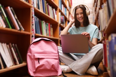 Photo of Student with laptop and backpack between shelves in library
