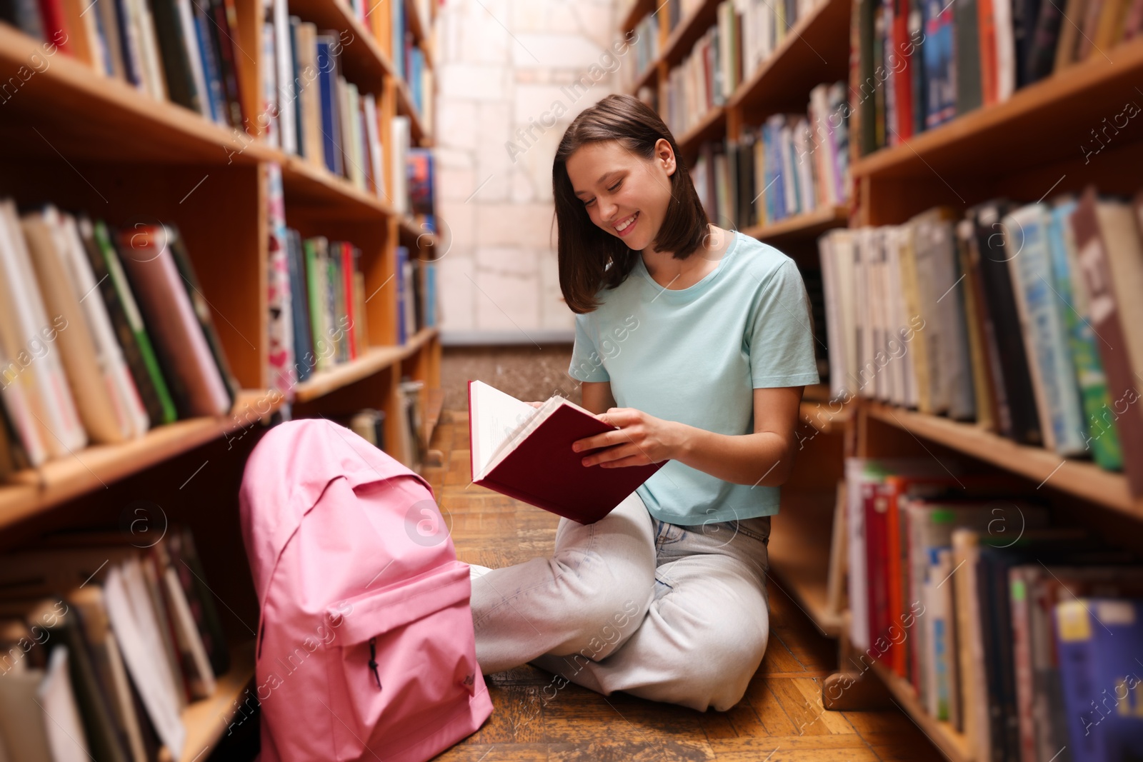 Student reading book on floor in library Photo of Student reading book on floor in library
