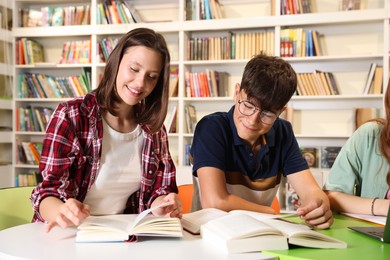 Photo of Students with books studying together at table in library