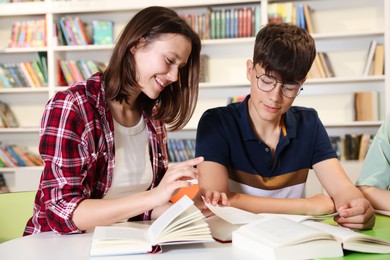 Photo of Students with books studying together at table in library