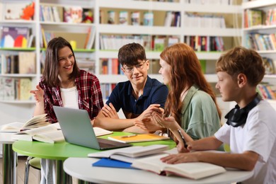 Photo of Students with books and laptop studying together at table in library