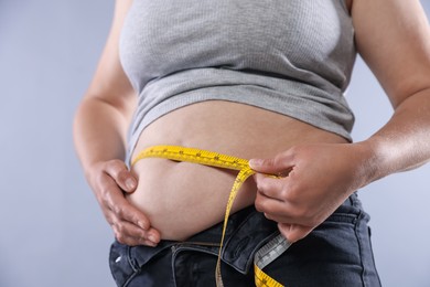 Photo of Overweight woman measuring her belly with tape on light background, closeup
