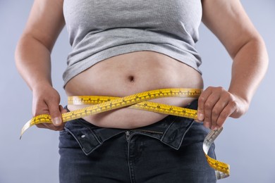Photo of Overweight woman measuring her belly with tape on light background, closeup