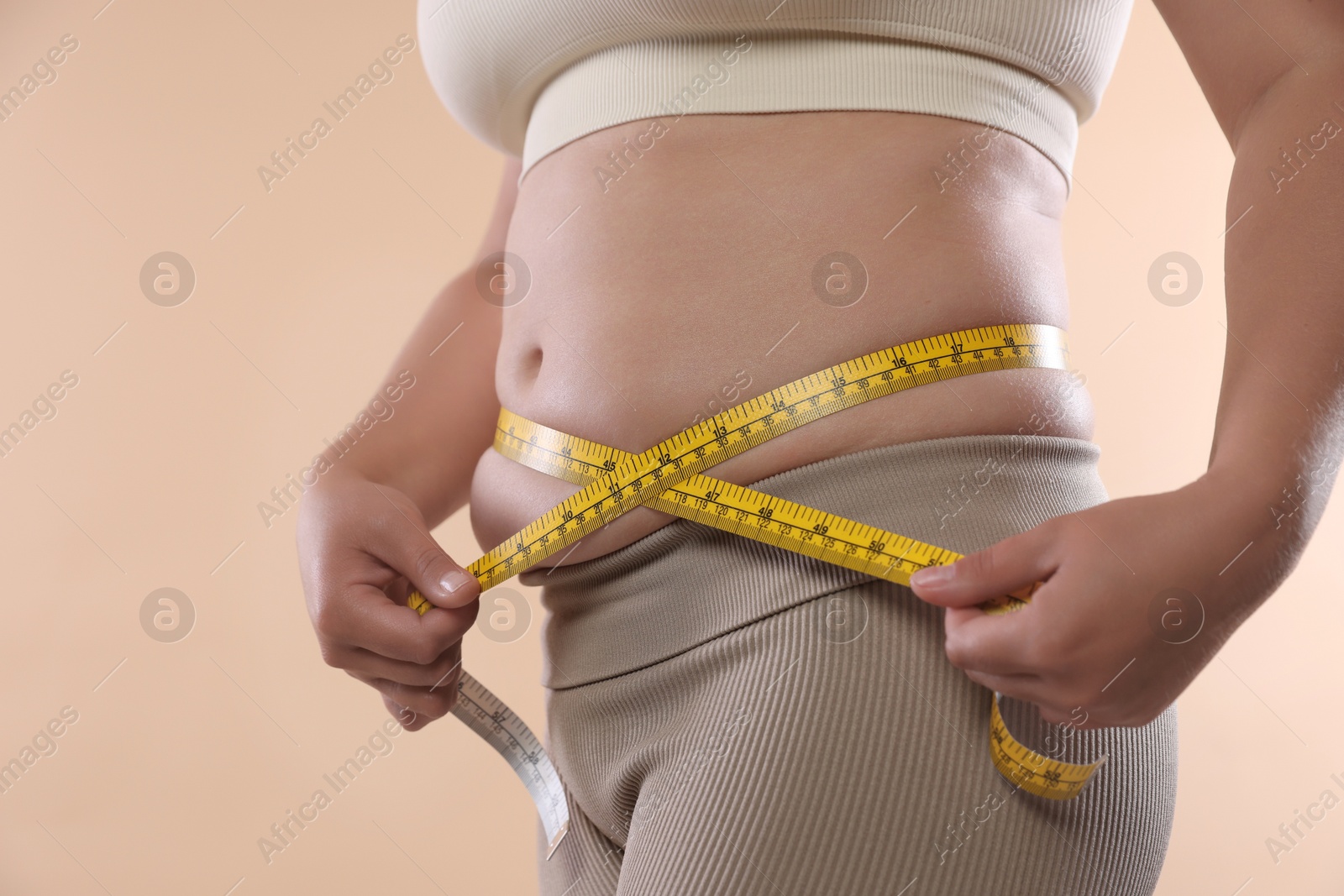 Overweight woman measuring her belly with tape on beige background, closeup Photo of Overweight woman measuring her belly with tape on beige background, closeup