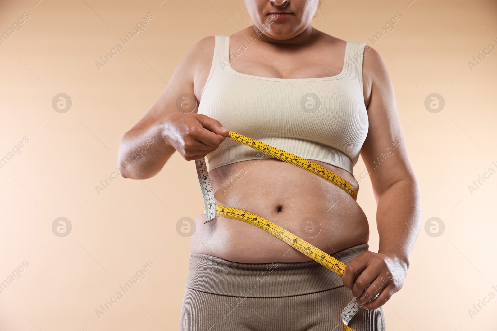 Overweight woman measuring her belly with tape on beige background, closeup Photo of Overweight woman measuring her belly with tape on beige background, closeup