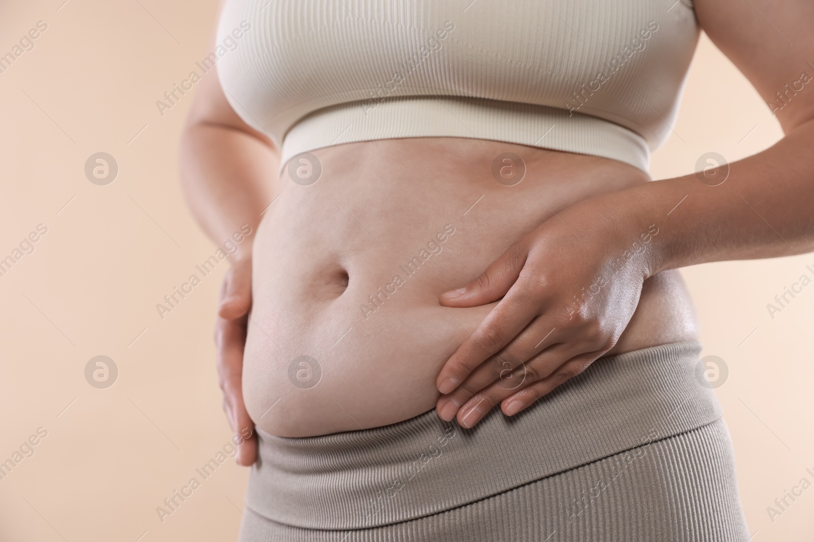 Woman with excessive belly fat on beige background, closeup. Overweight problem Photo of Woman with excessive belly fat on beige background, closeup. Overweight problem