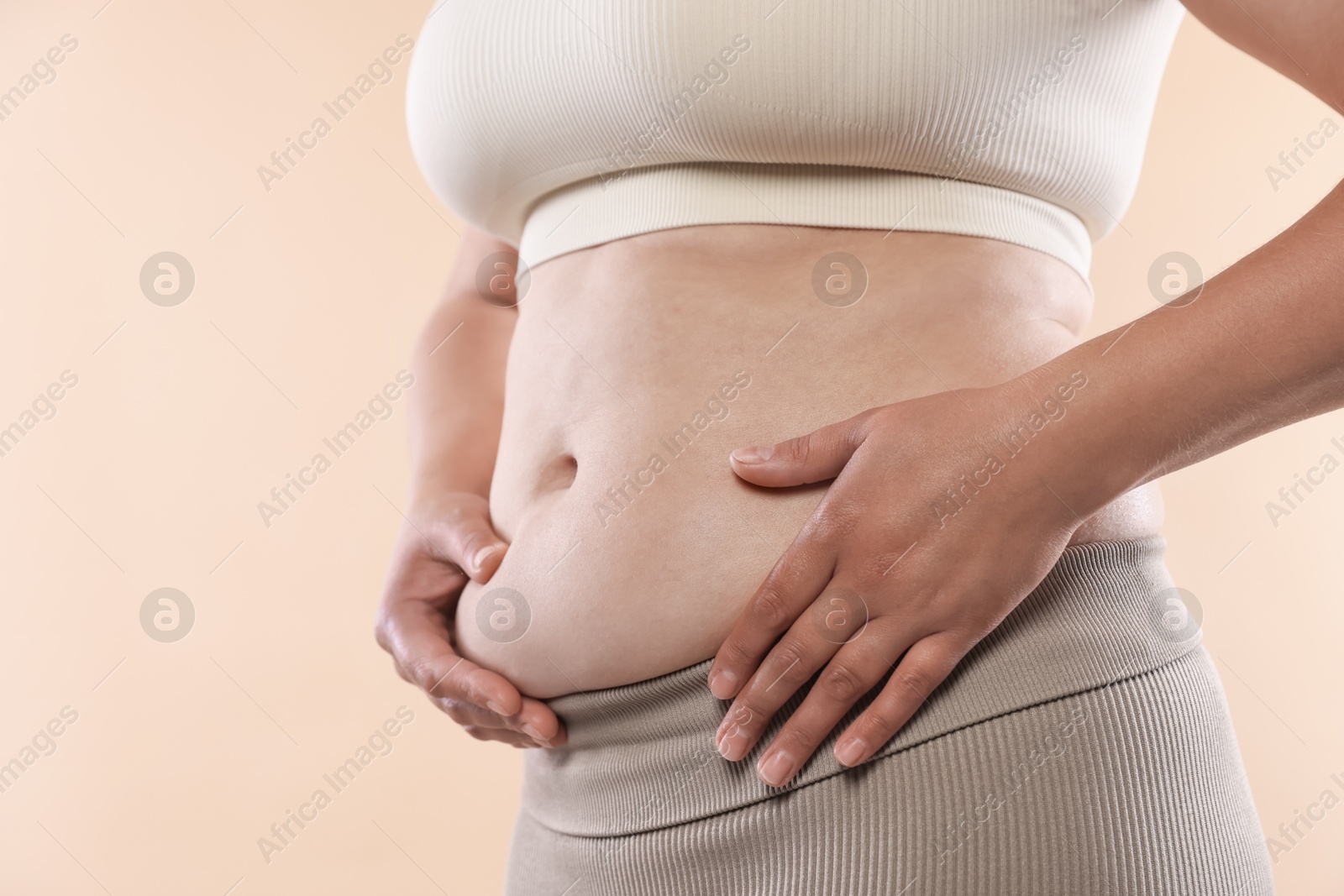 Woman with excessive belly fat on beige background, closeup. Overweight problem Photo of Woman with excessive belly fat on beige background, closeup. Overweight problem