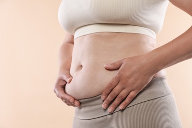 Photo of Woman with excessive belly fat on beige background, closeup. Overweight problem