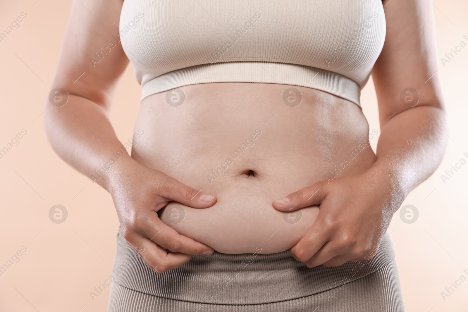Woman with excessive belly fat on beige background, closeup. Overweight problem Photo of Woman with excessive belly fat on beige background, closeup. Overweight problem