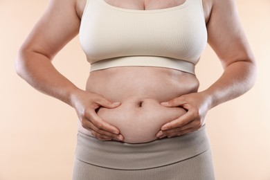 Photo of Woman with excessive belly fat on beige background, closeup. Overweight problem