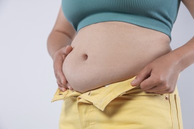 Photo of Woman with excessive belly fat on light background, closeup. Overweight problem
