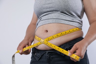 Photo of Overweight woman measuring her belly with tape on light background, closeup