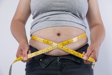 Photo of Overweight woman measuring her belly with tape on light background, closeup