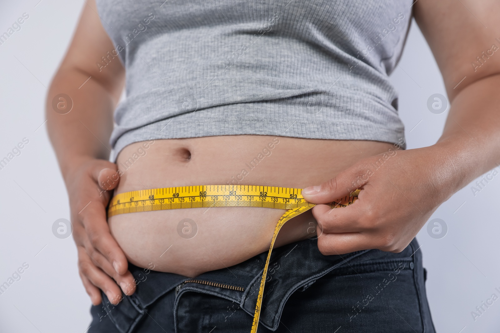 Overweight woman measuring her belly with tape on light background, closeup Photo of Overweight woman measuring her belly with tape on light background, closeup