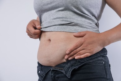 Photo of Woman with excessive belly fat on light background, closeup. Overweight problem