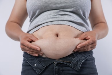 Photo of Woman with excessive belly fat on light background, closeup. Overweight problem