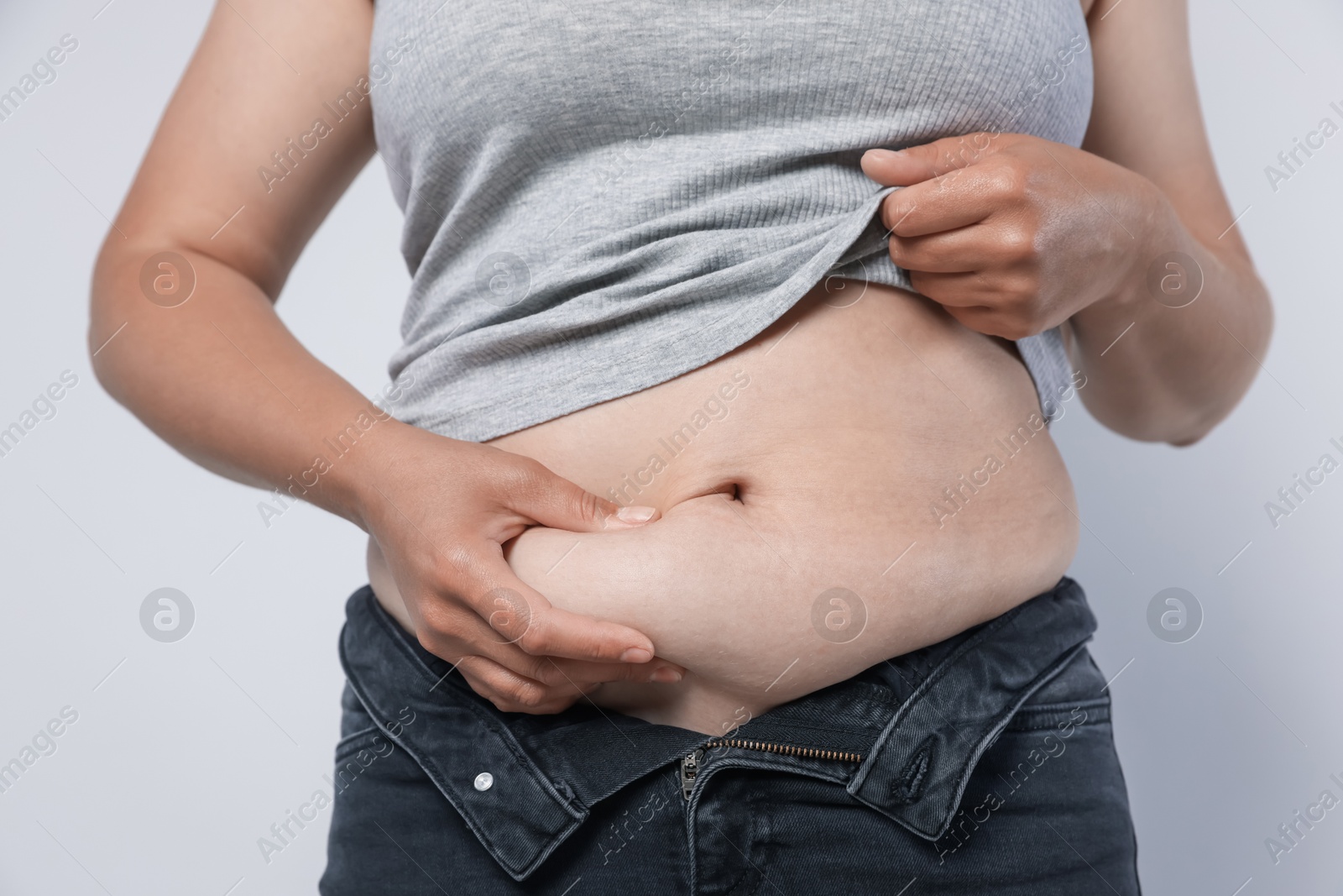 Woman with excessive belly fat on light background, closeup. Overweight problem Photo of Woman with excessive belly fat on light background, closeup. Overweight problem