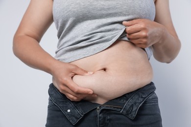 Photo of Woman with excessive belly fat on light background, closeup. Overweight problem
