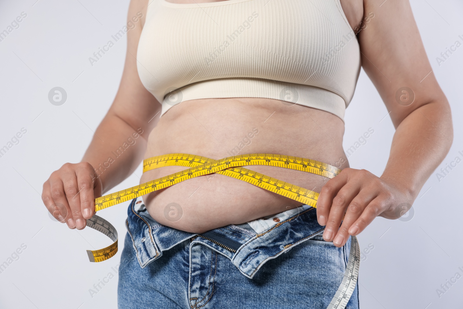 Overweight woman measuring her belly with tape on light background, closeup Photo of Overweight woman measuring her belly with tape on light background, closeup