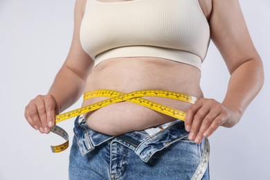 Photo of Overweight woman measuring her belly with tape on light background, closeup