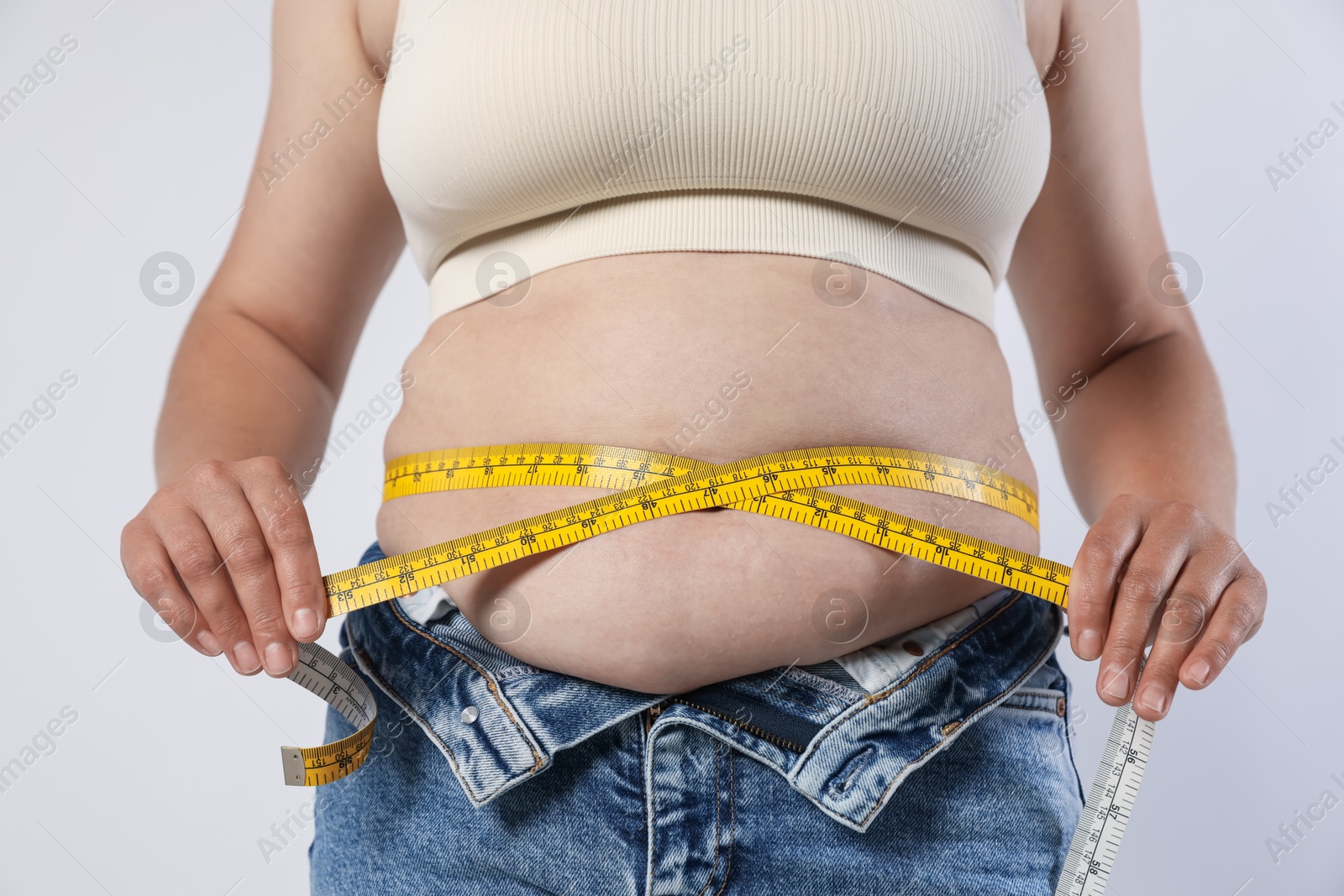 Overweight woman measuring her belly with tape on light background, closeup Photo of Overweight woman measuring her belly with tape on light background, closeup